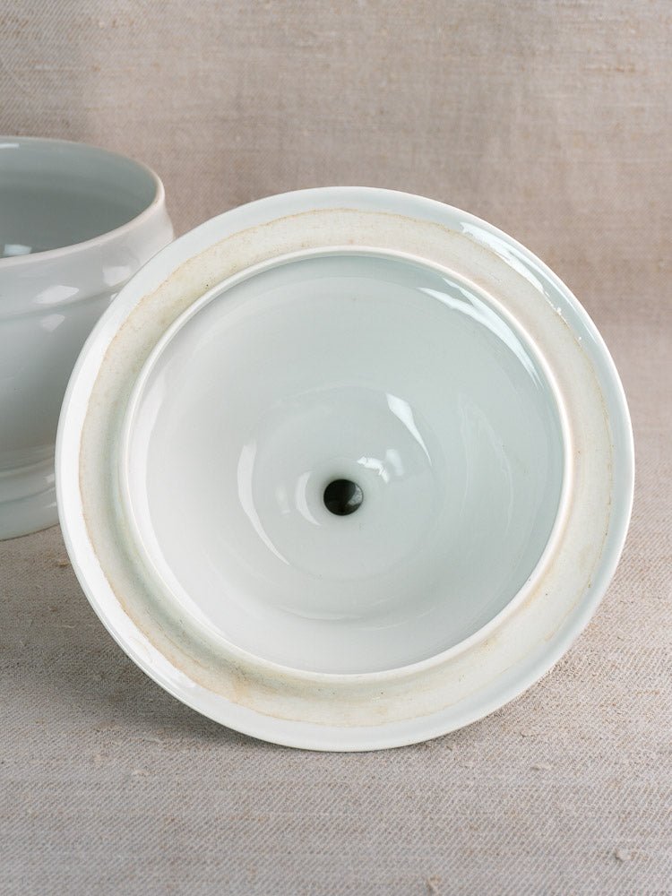 White porcelain lion head soup bowl from a vintage French tureen set, shown upside down on beige textured surface.