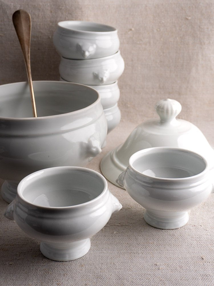 Vintage French CNP porcelain soup service with tureen and twelve lion head bowls on beige fabric.