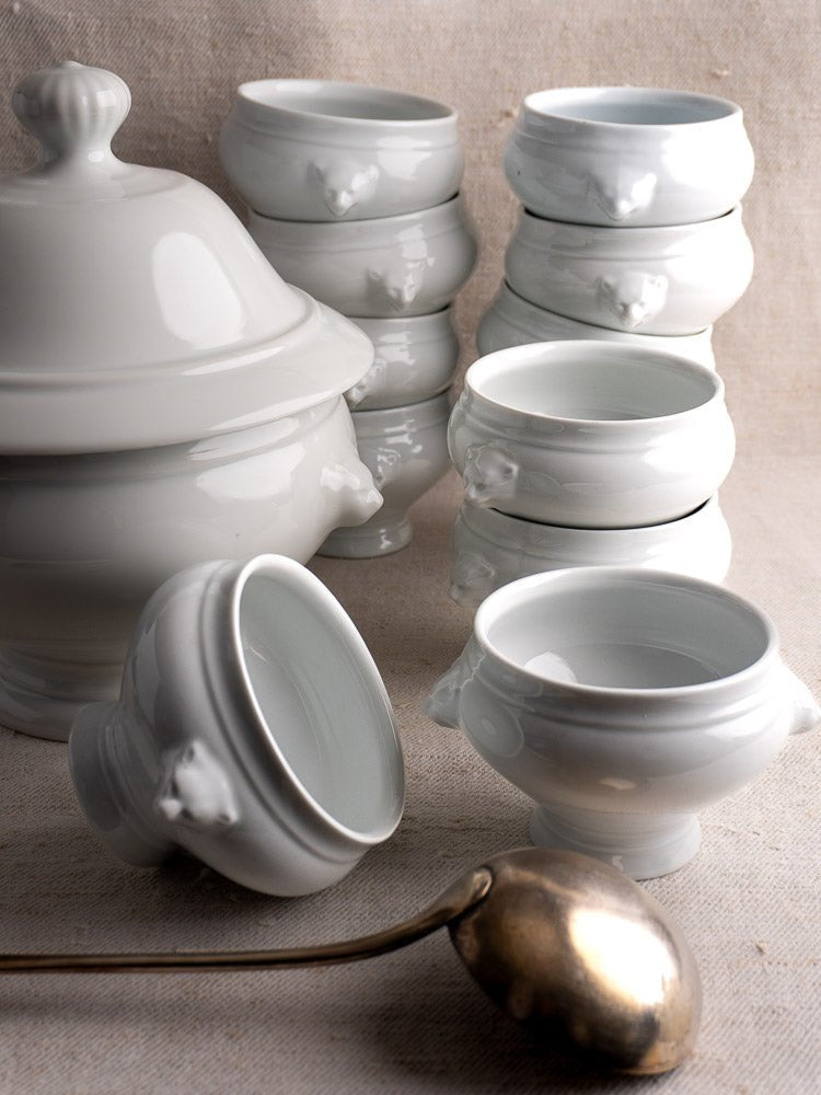 Vintage French CNP white ceramic tureen and twelve lion head bowls with metal ladle on fabric.