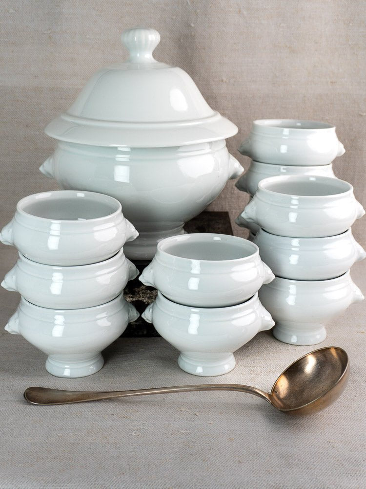 Vintage French CNP Soup Service with lidded tureen, twelve lion head bowls, and silver ladle on neutral cloth.
