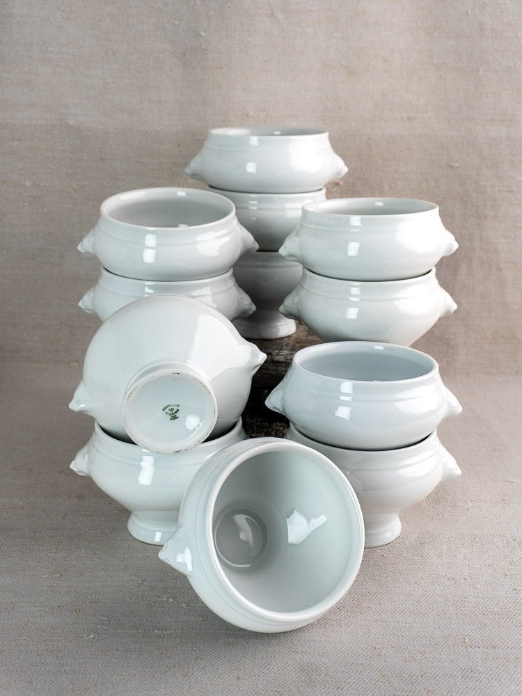 Set of twelve vintage French CNP lion head bowls with matching tureen on neutral fabric backdrop.