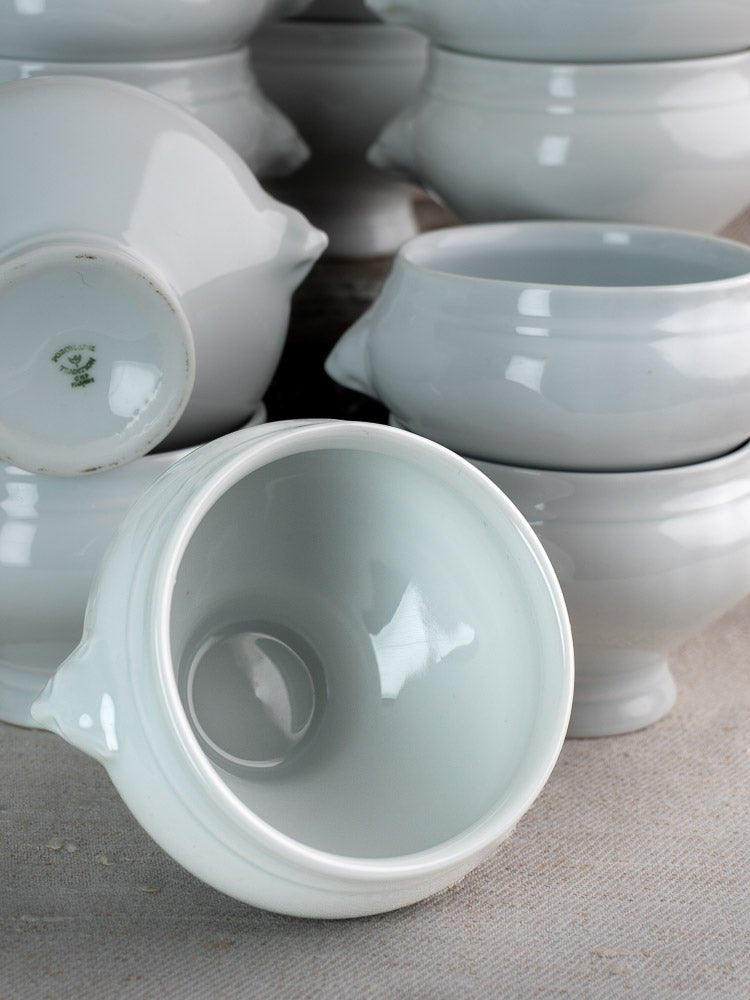 Stacked white vintage French CNP soup lion head bowls, one showing glossy interior on light fabric.