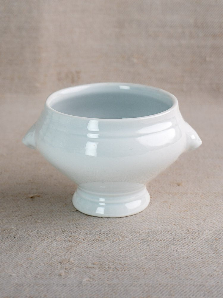Vintage French CNP lion head soup bowl in white ceramic with twin handles on beige surface.