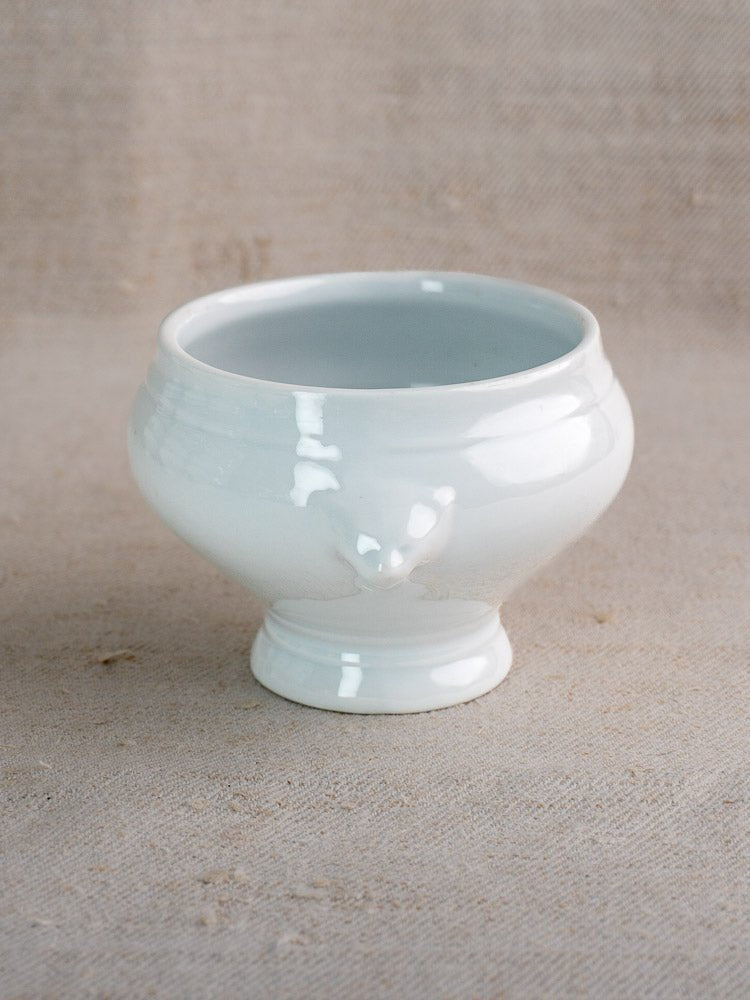 White vintage French lion head soup bowl with glossy finish on a textured beige surface.