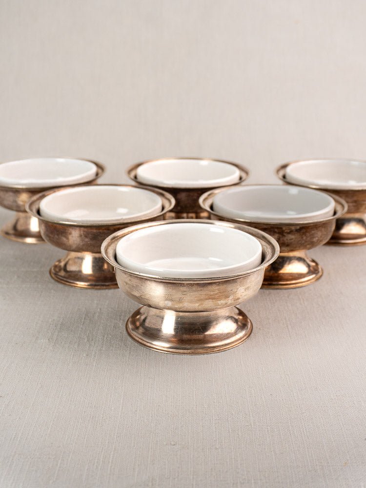 Set of six vintage Sambonet silver plate coupes with white porcelain inserts, artfully grouped on a neutral surface.
