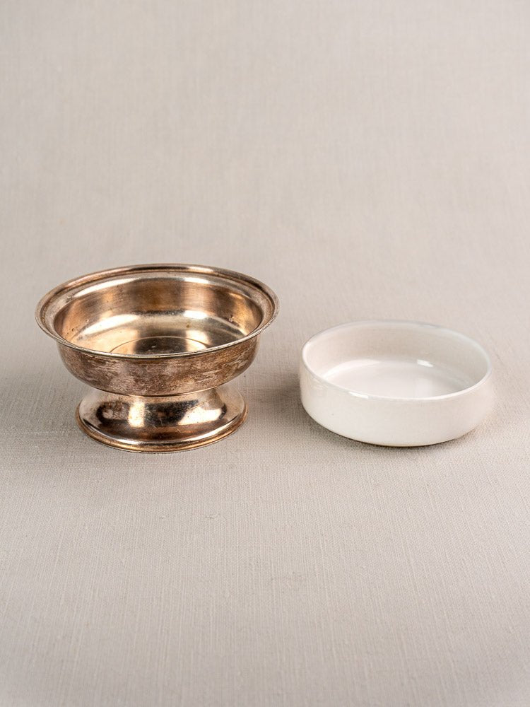 Silver-plated vintage Sambonet coupe with wide rim beside a small white ceramic dish on fabric.