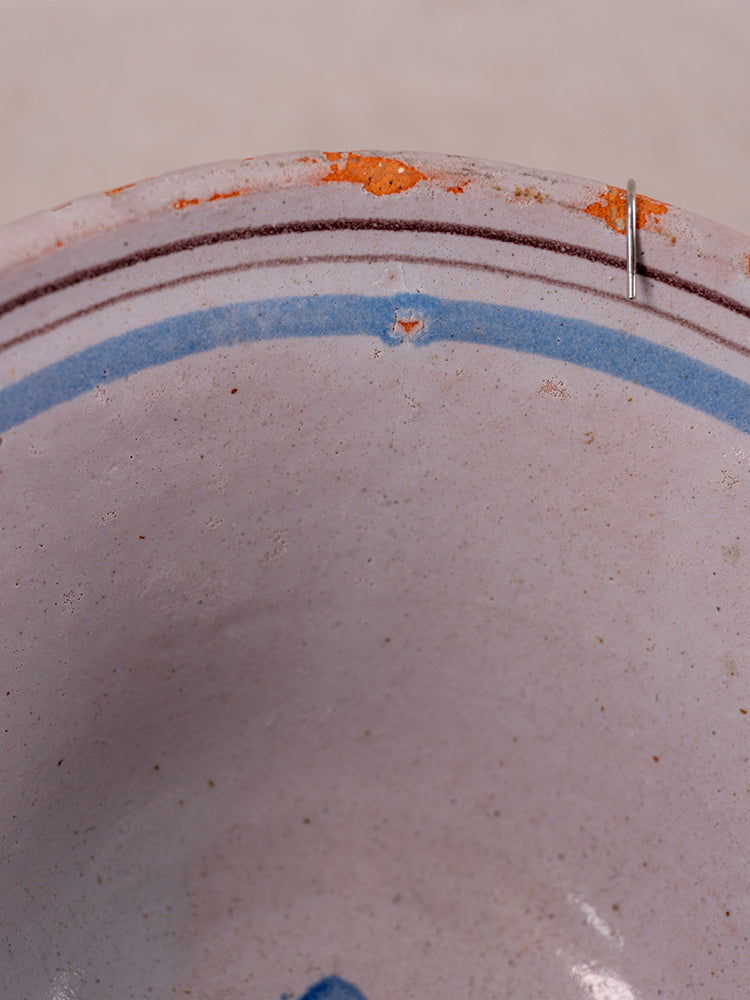 Antique French Cul Noir faience bowl with blue floral motifs, chipped rim, orange staining, and staple repair.