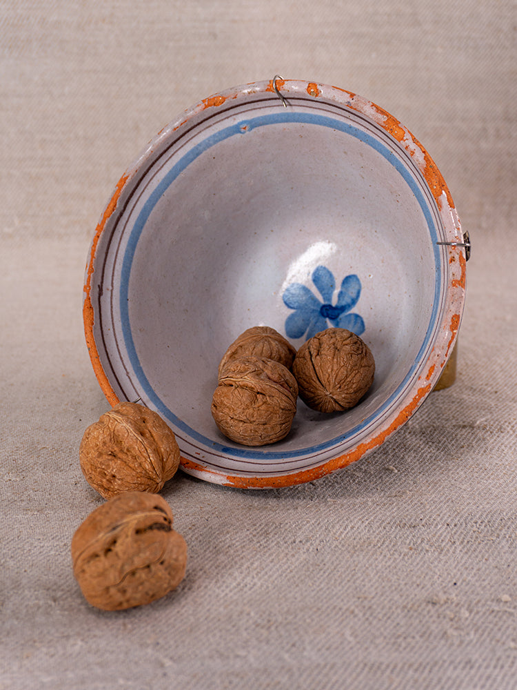 Antique French cul noir faience bowl with blue floral motifs and orange rim, tipped on fabric, spilling walnuts.