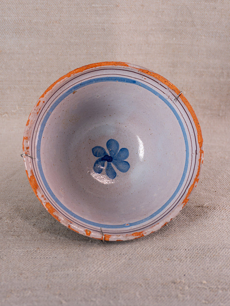 19th century French cul noir faience bowl, hand-painted blue floral motif, worn clay edges, on neutral textured fabric.