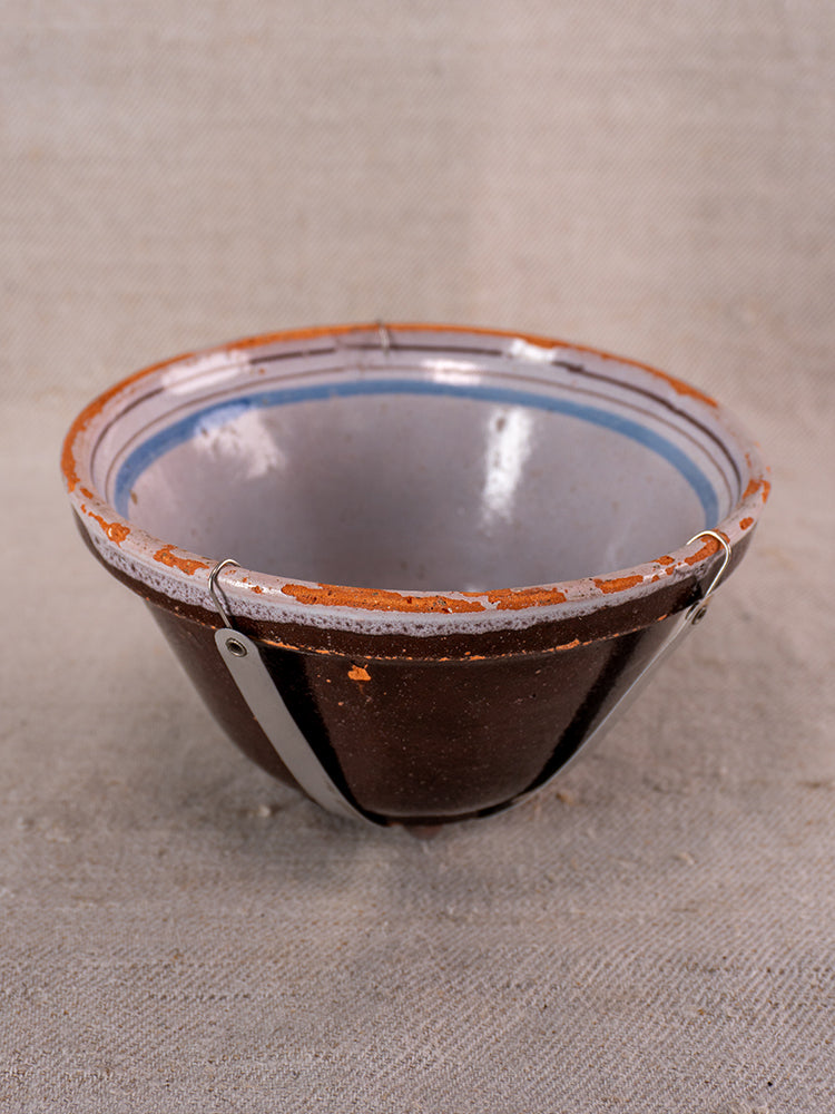 19th century French Cul Noir faience bowl, hand-painted blue floral interior, brown exterior, metal rim clips on beige fabric.