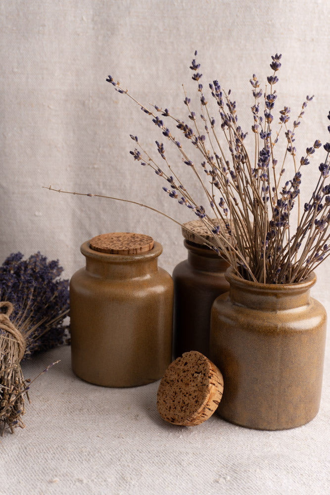 Set of three mid-20th century French stoneware mustard pots with cork lids in earthy brown tones on beige fabric.