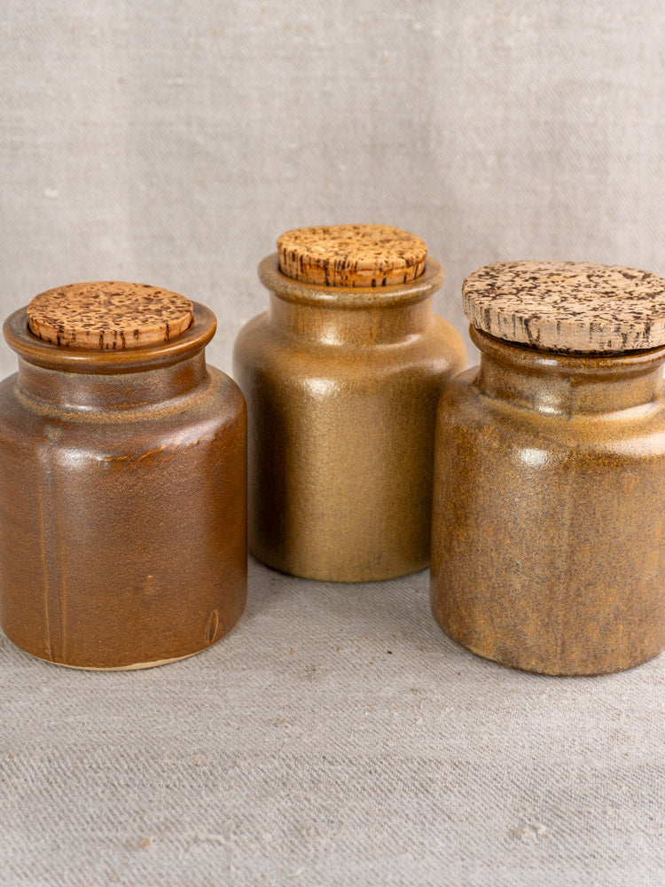 Set of three mid-century French stoneware mustard pots with cork lids and varied brown glazes.