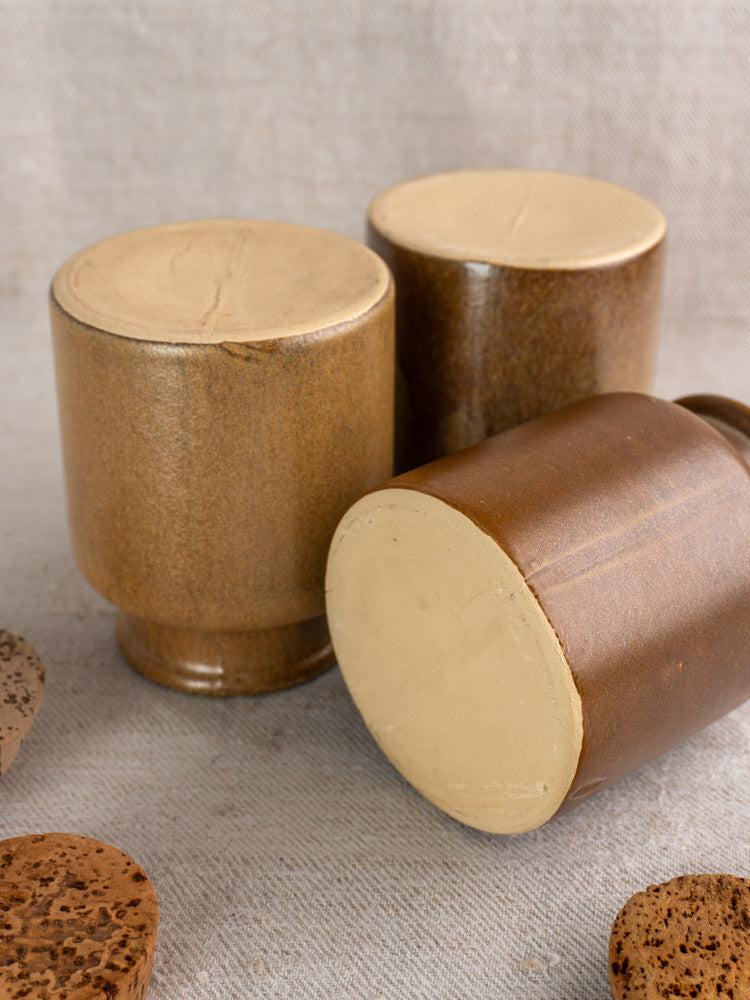 Set of three mid-20th century French stoneware mustard pots with cork lids on textured beige surface.