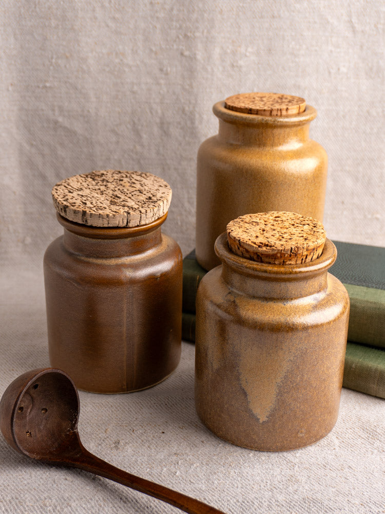 Set of three mid-century French stoneware mustard pots with cork lids on beige fabric, rustic brown tones.