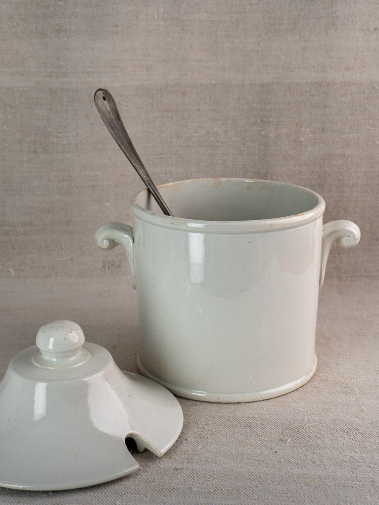 White Antique French Lunéville faience soup tureen with lid, handles, and spoon, on textured fabric background.