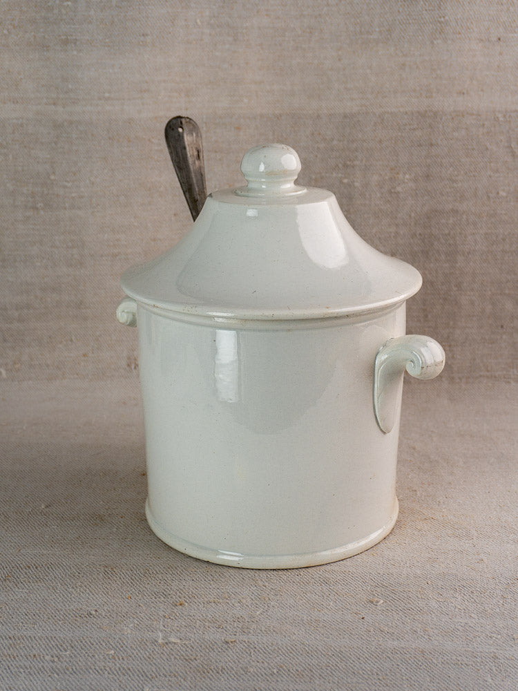 Antique French Lunéville white faience soup tureen with lid, handles, and metal spoon on fabric.