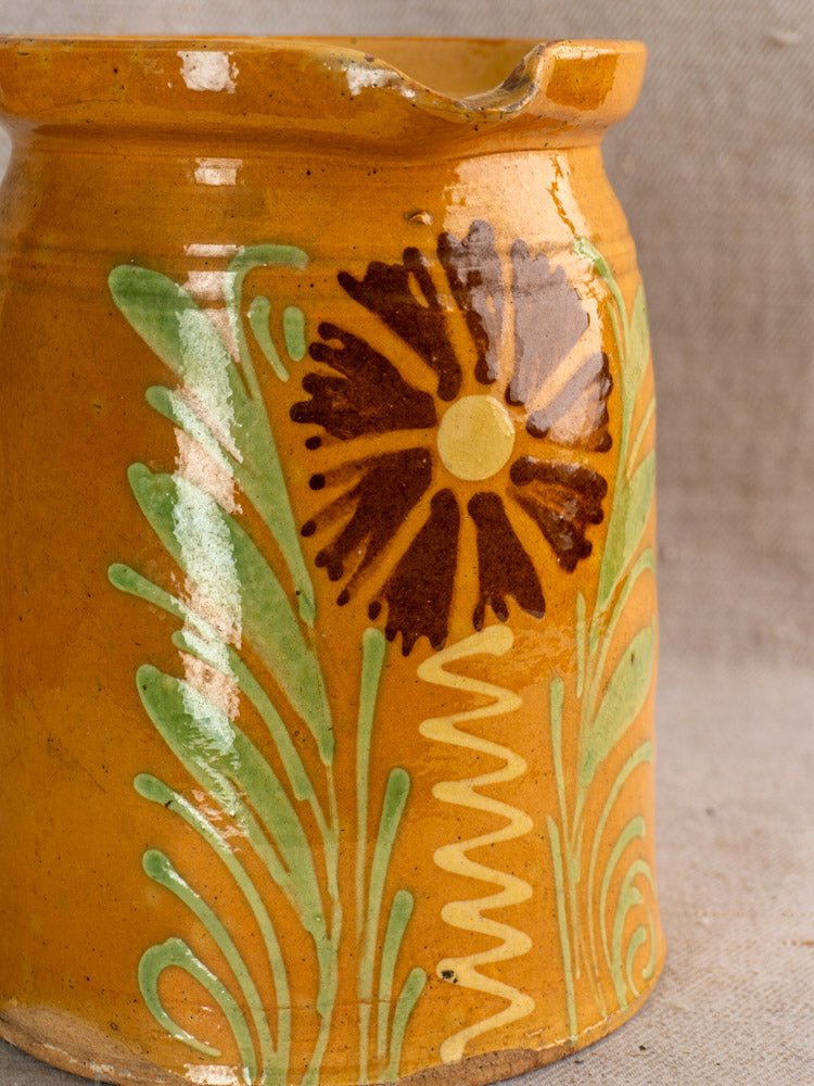Antique French Savoyard pitcher with yellow ochre glaze, hand-painted floral motif, on fabric background.