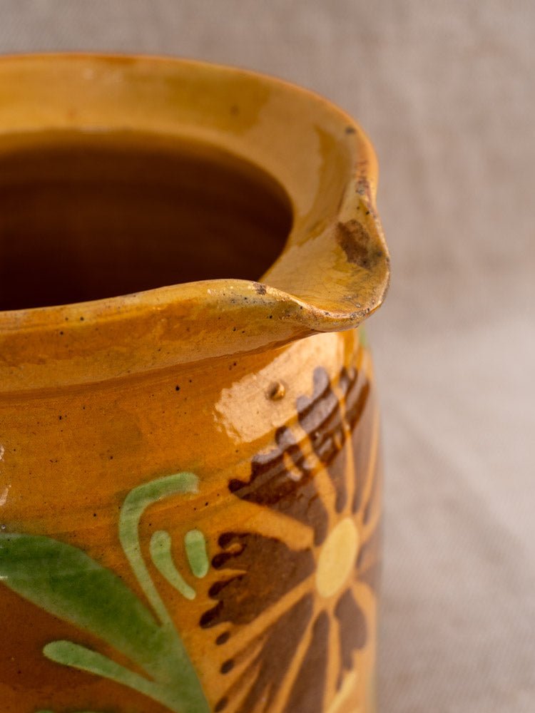 Antique French Savoyard pitcher with chipped spout, hand-painted yellow and brown floral design, ochre glaze; neutral fabric backdrop.