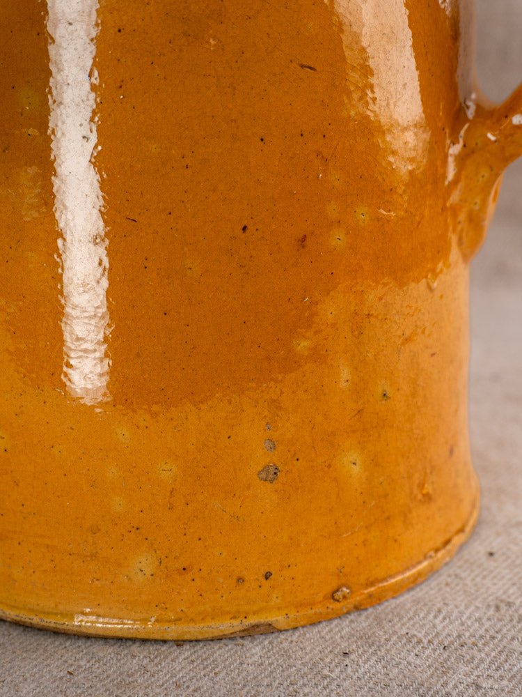 Antique French Savoyard ceramic pitcher with glossy orange glaze, yellow ochre accents, on gray textured background.