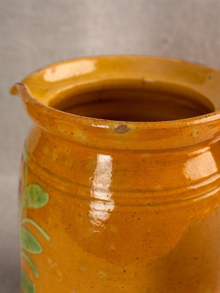 Antique French Savoyard pitcher with yellow ochre glaze, hand-painted florals, chip on rim, neutral background.