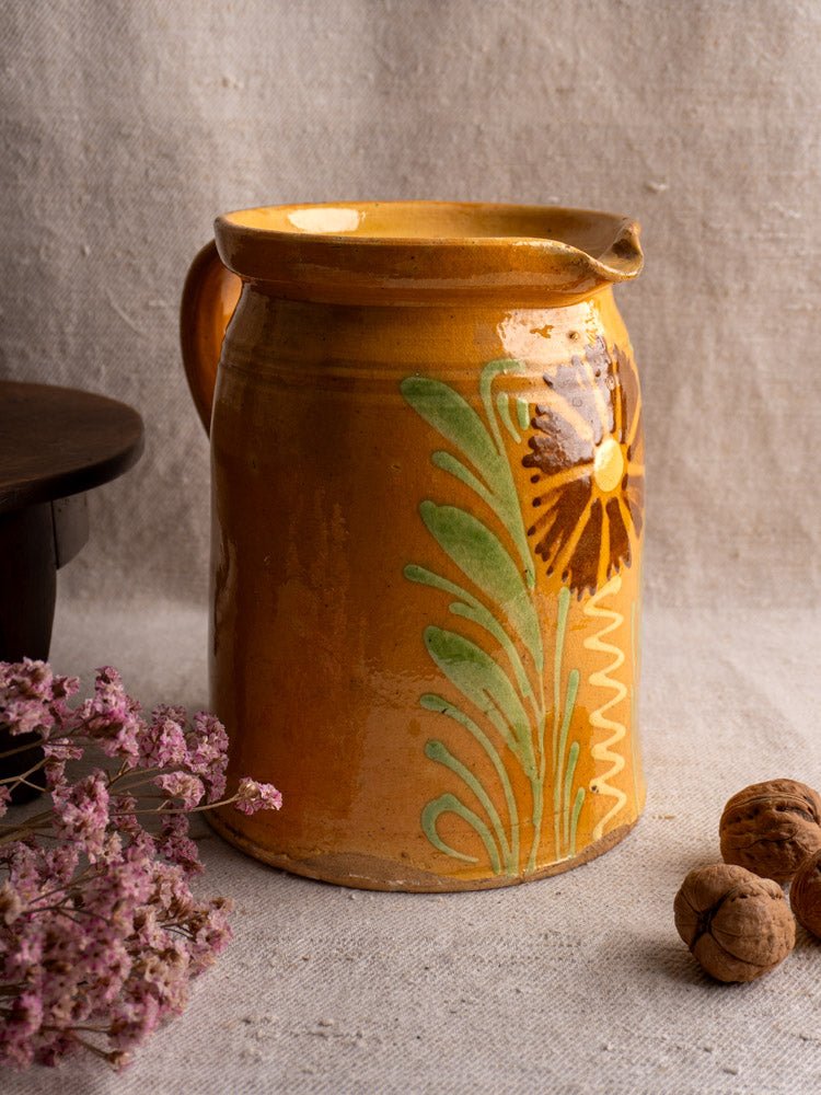 Antique French Savoyard pitcher with yellow ochre glaze and floral designs on beige cloth with dried flowers.