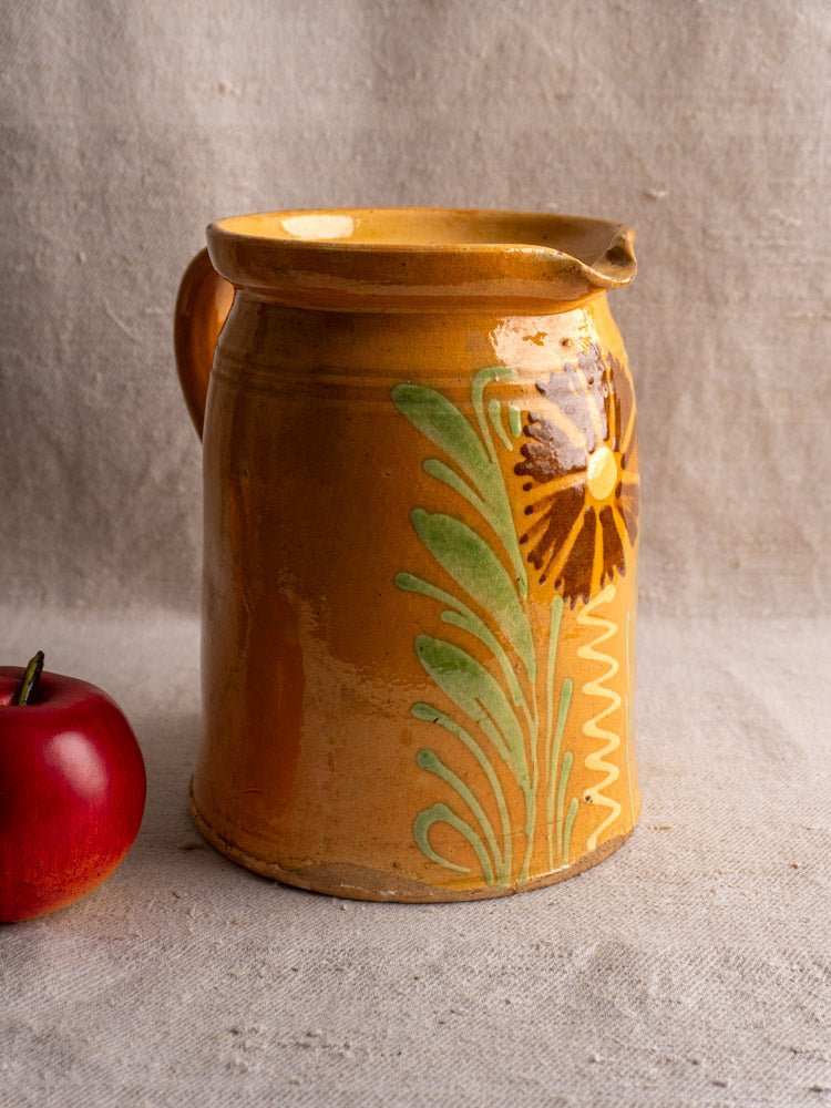Antique French Savoyard pitcher with yellow ochre glaze and floral design beside a red apple.