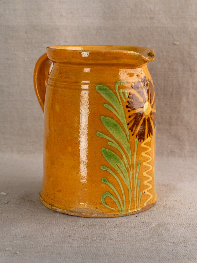 Antique French Savoyard ceramic pitcher with handle, yellow ochre glaze, green leaves, brown flower on fabric.