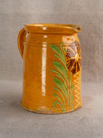 Antique French Savoyard ceramic pitcher with handle, yellow ochre glaze, green leaves, brown flower on fabric.