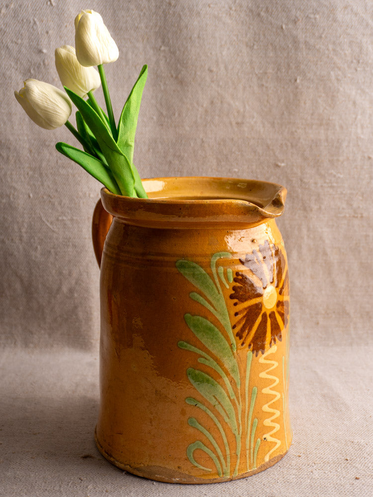 Antique French Savoyard ceramic pitcher with handle, yellow ochre glaze, green leaves, brown flower on fabric.