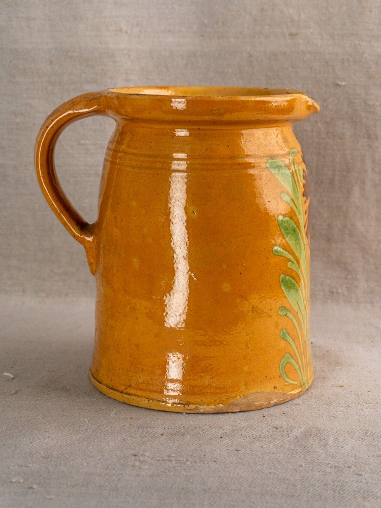 Antique French Savoyard-style pitcher with yellow ochre glaze and floral motifs on neutral fabric background.