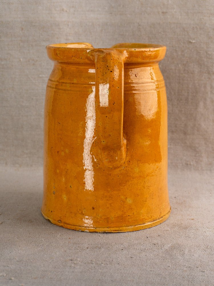 Antique French Savoyard pitcher with yellow ochre glaze, hand-painted florals, single handle, on neutral fabric.
