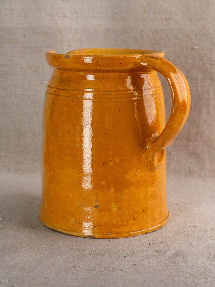 Antique French Savoyard pitcher with yellow ochre glaze and hand-painted floral details on beige cloth.
