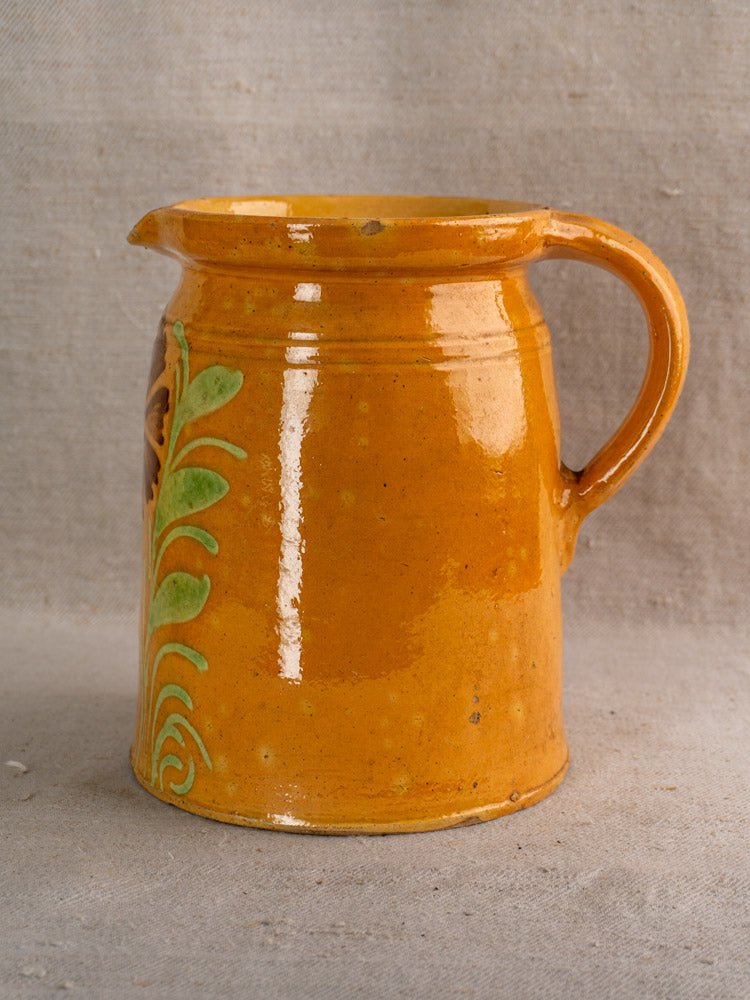 Antique French Savoyard pitcher with yellow ochre glaze, floral accents, orange-brown handle on fabric background.