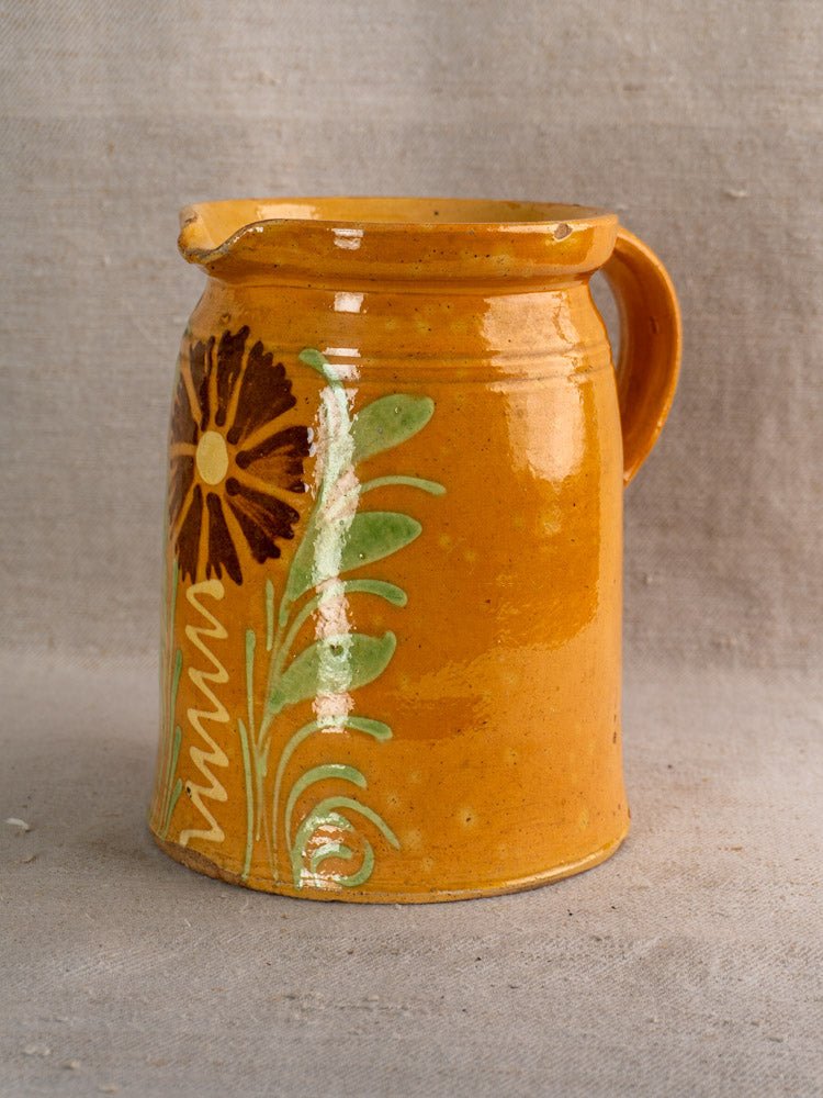 Antique French Savoyard ceramic pitcher with yellow ochre glaze and hand-painted floral motif on gray fabric.