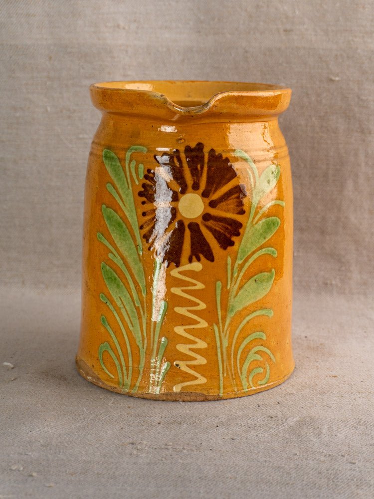 Antique French Savoyard pitcher with yellow ochre glaze, brown flower and green leaf motifs on textured fabric.