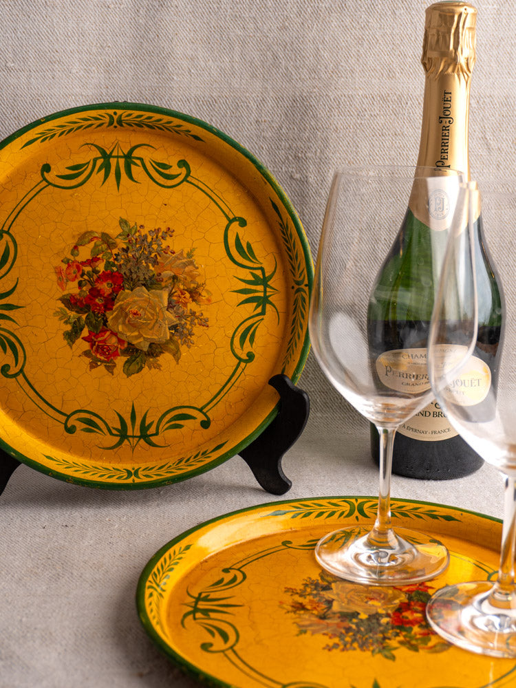 Pair of antique French painted tôle trays with floral motifs, shown with champagne and wine glasses.