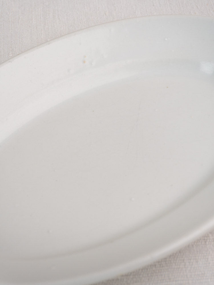 Pair of antique French white ironstone oval platters with glossy surfaces on textured fabric.