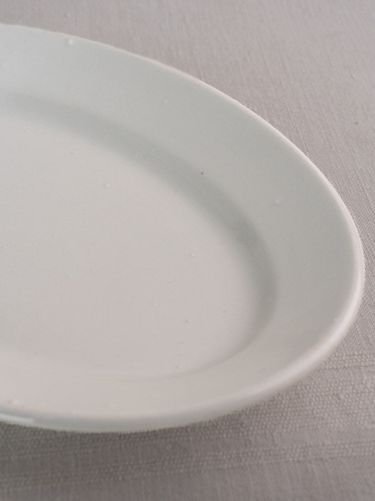 Pair of antique French white ironstone oval platters in graduated sizes on beige tablecloth.