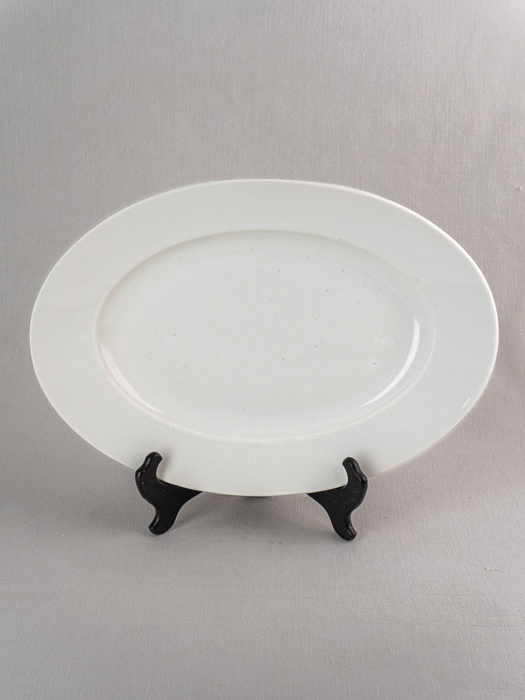 Pair of antique French white ironstone oval platters in graduated sizes on black wire stand.