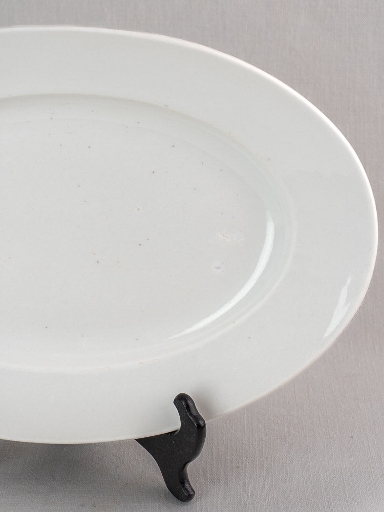 Pair of antique French white ironstone oval platters with subtle glaze specks on a black wire stand.