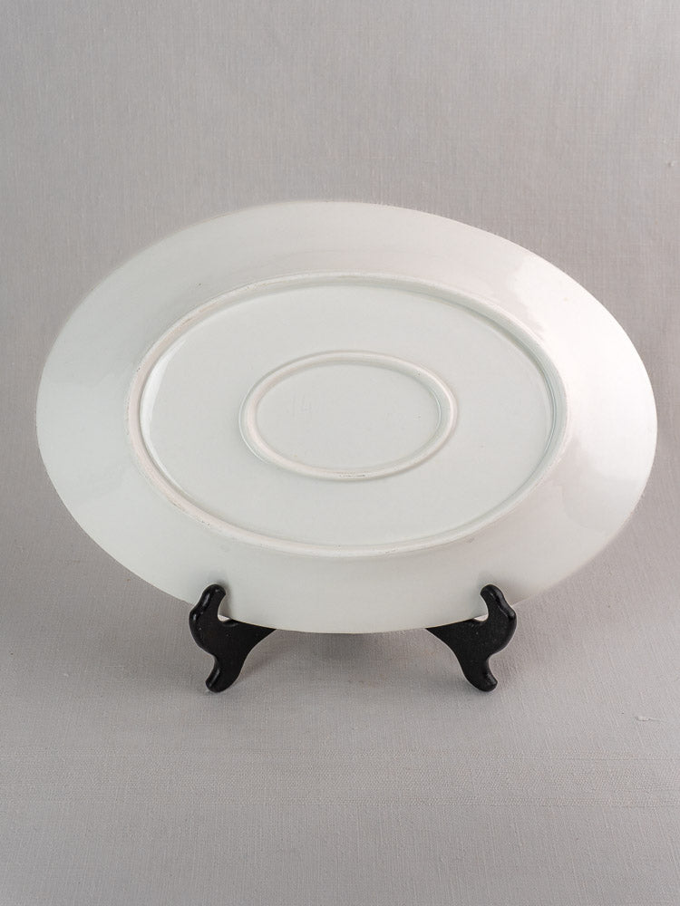 Antique French white ironstone oval platter back on black stand, neutral gray background.