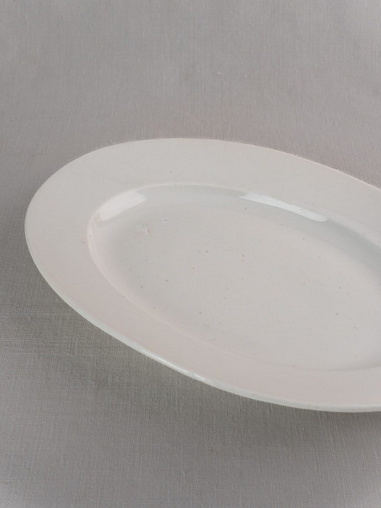 Pair of antique French white ironstone oval platters in graduated sizes on light gray surface.