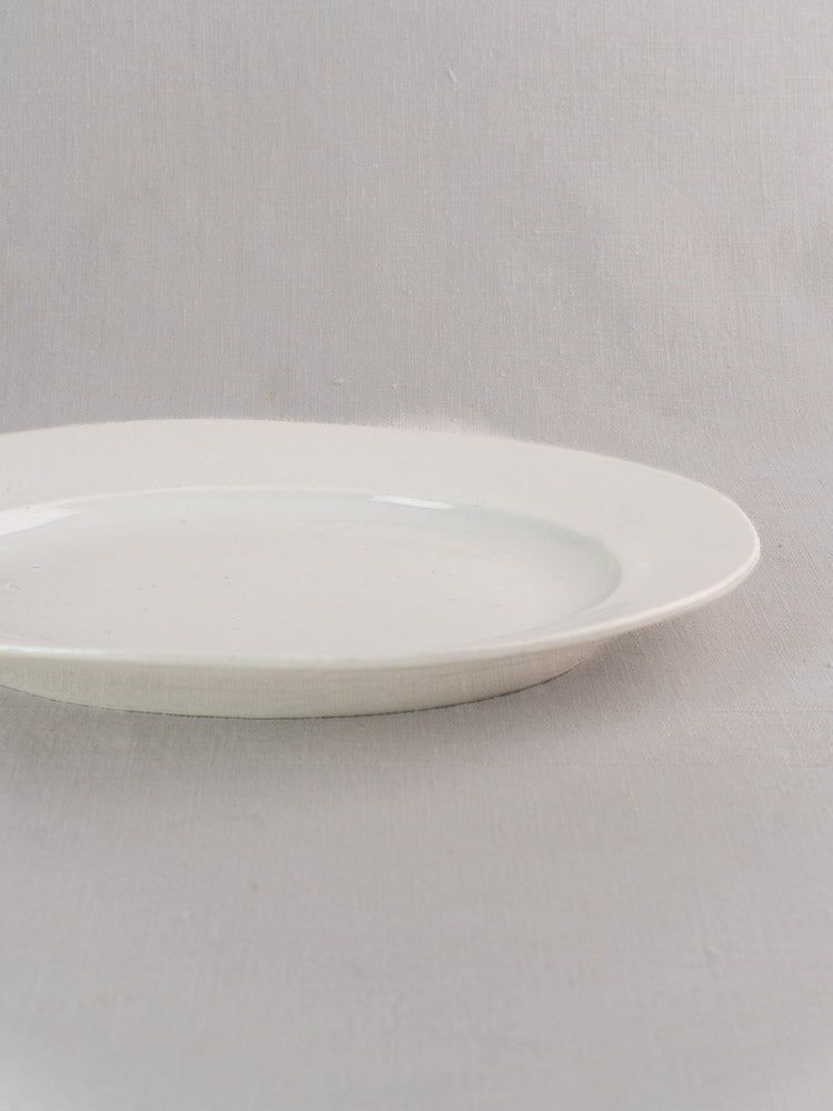 Antique French white ironstone oval platters in graduated sizes on a light gray fabric surface.