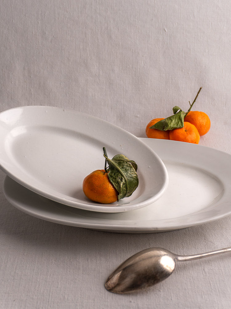 Pair of antique French white ironstone oval platters in graduated sizes on black stands, gray background.