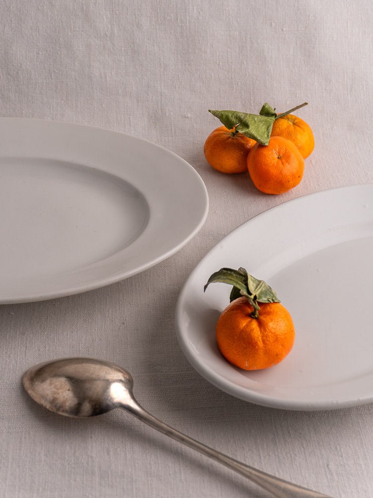 Pair of antique French white ironstone oval platters with tangerines and silver spoon on linen.