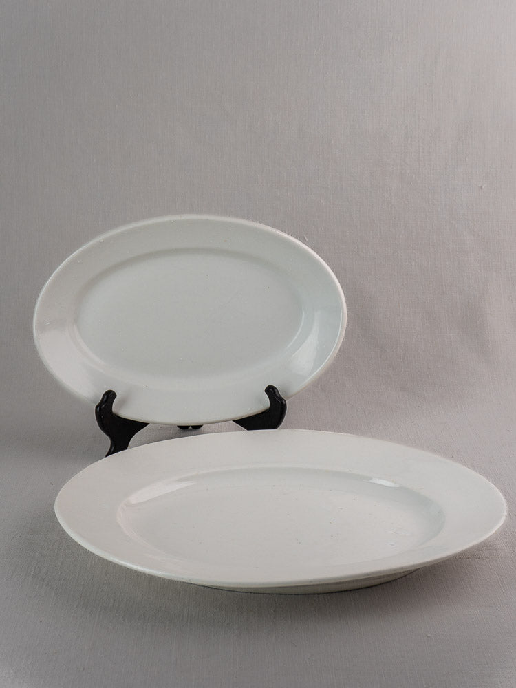 Antique French white ironstone oval platters, graduated sizes, one upright on stand, one flat.