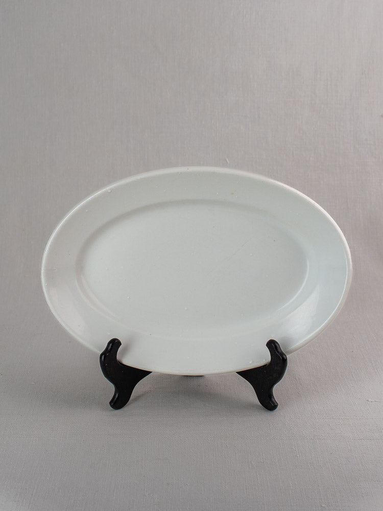 Pair of antique French white ironstone oval platters in graduated sizes on black stand, grey background.