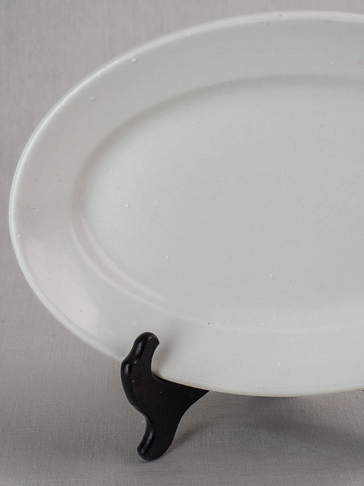 Pair of antique French white ironstone oval platters, graduated sizes, on black stand, light gray background.