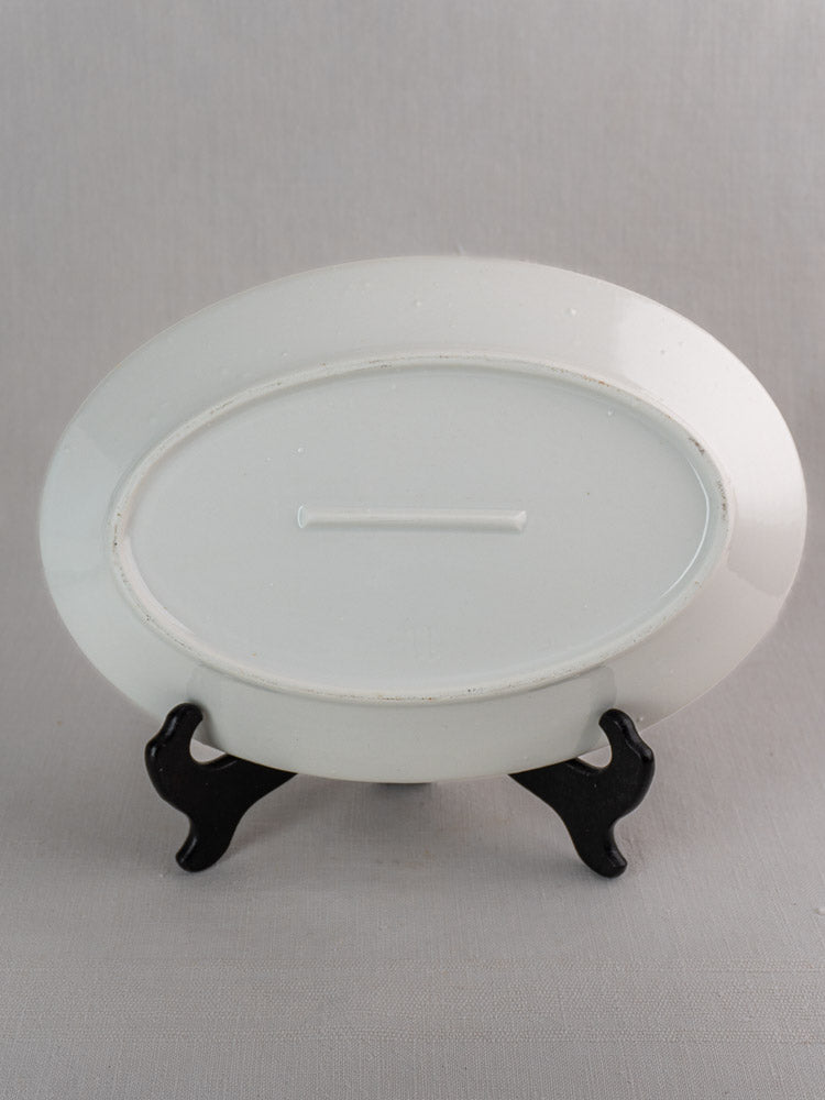 Antique French white ironstone oval platters in two sizes, displayed bottoms up on a black stand, gray backdrop.