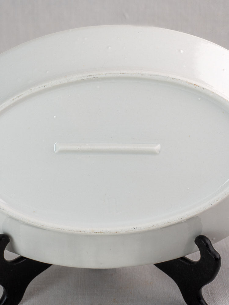 Antique French white ironstone oval platter upside down on black stand, plain background.